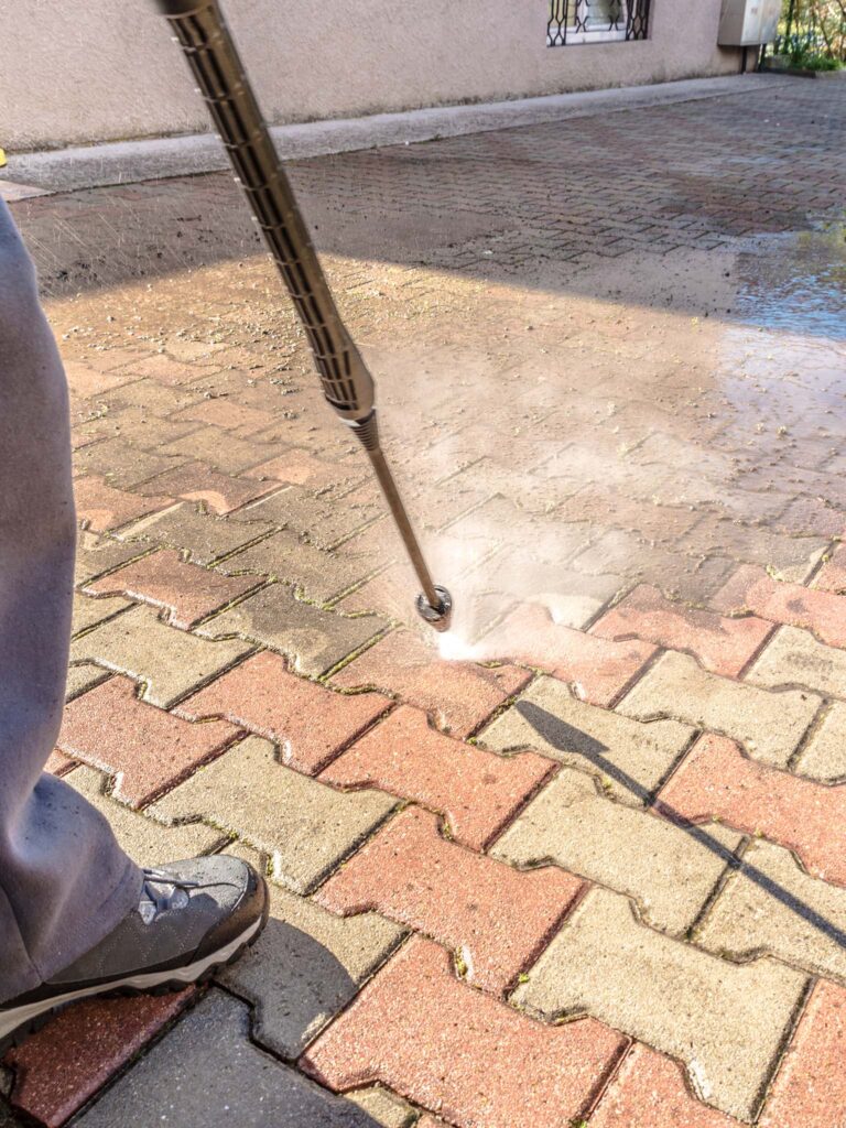A Person Using A Pressure Washer To Clean A Brick Sidewalk