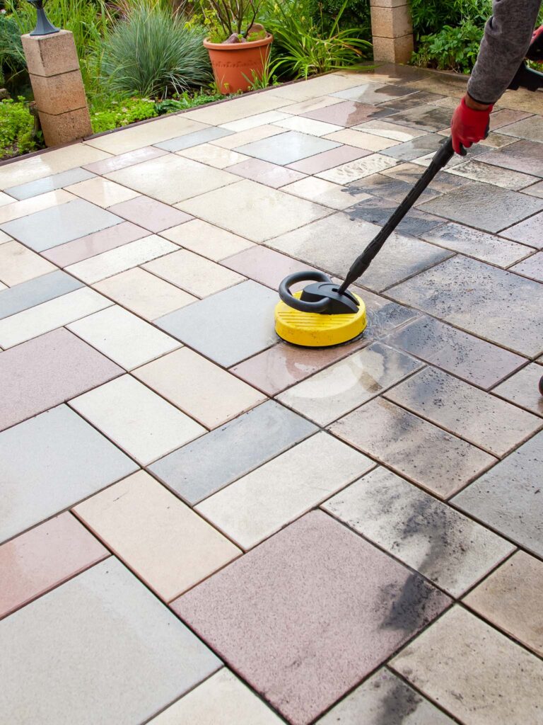 A Person Cleaning A Patio With A Yellow Pressure Washer